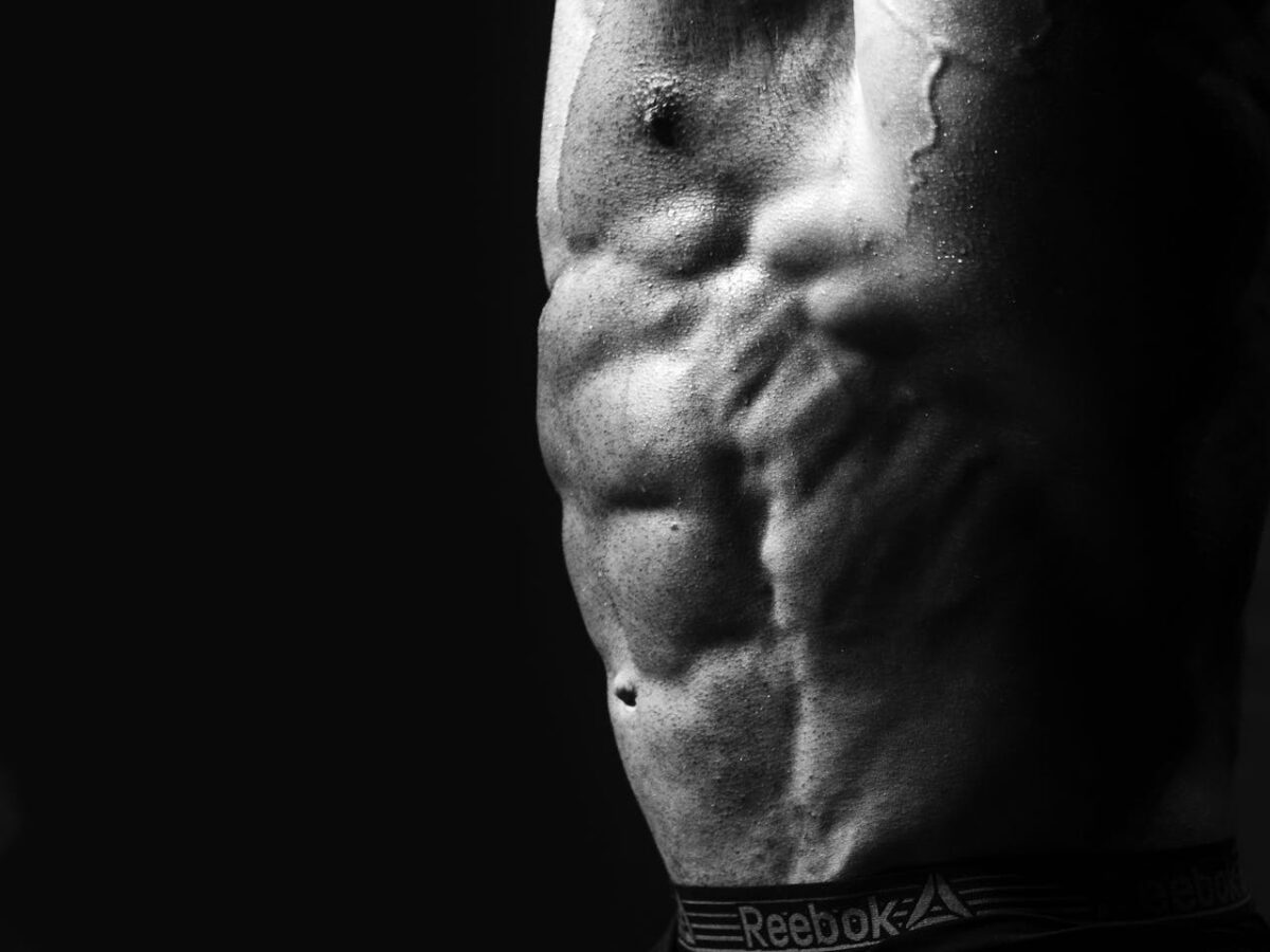 Dramatic black and white photo of a muscular male torso highlighting defined abs.